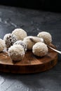 Sweet energy balls with coconut flakes in pile on dark oak slab with silver spon on black background