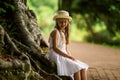 Sweet girl in a hat and white dress walks in the botanical garden on a summer day