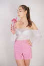 Sweet girl in transparent blouse, summer funny plaid shorts and pink high heels posing with a glass cup of water on white backgrou Royalty Free Stock Photo