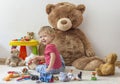 Sweet happy child boy having fun playing with his giant teddy bear and many colorful toys, indoor at home Royalty Free Stock Photo