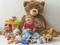 Sweet happy child boy having fun playing with his giant teddy bear and many colorful toys, indoor at home Royalty Free Stock Photo