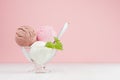 Sweet ice cream balls - strawberry, chocolate, creamy in elegant transparent glass bowl with spoon, green mint on white wood table