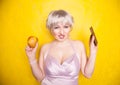 Sweet joyous curvaceous girl with a short haircut stands in a delicate evening silk dress and compares bad and good food