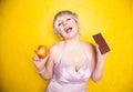 Sweet joyous curvaceous girl with a short haircut stands in a delicate evening silk dress and compares bad and good food Royalty Free Stock Photo