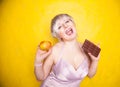 Sweet joyous curvaceous girl with a short haircut stands in a delicate evening silk dress and compares bad and good food Royalty Free Stock Photo