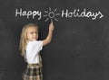 Sweet junior schoolgirl with blonde hair standing happy and smiling writing with chalk happy holidays Royalty Free Stock Photo