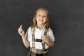 Sweet junior schoolgirl with blonde hair standing and smiling happy isolated in blackboard background