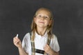 Sweet junior schoolgirl with blonde hair standing and smiling happy isolated in blackboard background