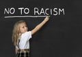 Sweet junior schoolgirl writing with chalk no to racism in school classroom blackboard