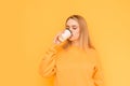 Sweet lady in an orange sweater drinks coffee from a paper cup with her eyes closed on a yellow background. Young coffee lover Royalty Free Stock Photo