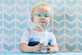 Sweet little boy drinking milk with funny glasses straw.