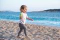 Sweet little caucasian baby girl with blond curly hair running,laughing on sandy beach by blue sea.Happy,adorable,cute Royalty Free Stock Photo