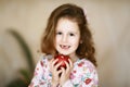 A sweet little curly tooth with brown eyes the girl smiles and holds in her hands a red apple that has lost milk teeth Royalty Free Stock Photo