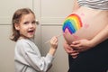 Sweet little daugter painting pregnant belly her mother. Pregnant mom and her child having fun together at home. Family, healthy