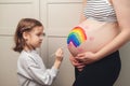 Sweet little daugter painting pregnant belly her mother. Pregnant mom and her child having fun together at home. Family, healthy