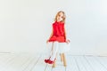 Sweet little girl in red dress sitting on chair against white wall at home, relaxing in white bright living room indoors. Royalty Free Stock Photo