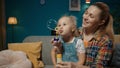 A sweet little girl sits on her mom's lap and blows soap bubbles. Mom and cute little daughter spending time Royalty Free Stock Photo