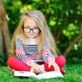 Sweet little girl wearing glasses and reading book in a park Royalty Free Stock Photo