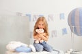 Sweet little redhead girl is hugging teddy bear on at home. Smiling little blonde girl holding toy on background of decorative bal Royalty Free Stock Photo