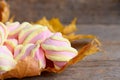 Fluffy yellow and pink marshmallows on yellow autumn leaves and on a vintage wooden table. Sweet marshmallow closeup