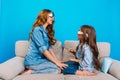 Sweet moments of pretty young mother having fun with daughter on couch on blue background. Fashionable outlook