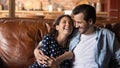 Bonding young spouses laugh hug on couch in playful mood