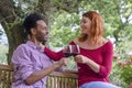 Sweet multiethic couple enjoying a glass of wine together outdoor in a garden sitting on bench. diverse happy friends having fun Royalty Free Stock Photo