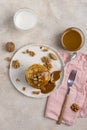 Sweet pancakes with boiled condensed milk and walnuts on plate with fork and knife, milk in glass and caramel in jar near, at