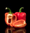 Sweet peppers, red, whole and cut into pieces, on a black background, with reflection Royalty Free Stock Photo