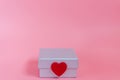 Sweet pink background with a silver gift box and decoration seal with a craft little red heart symbol of love and care. Valentines Royalty Free Stock Photo