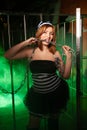 Sweet plus size woman in a carnival striped inmate costume stands near the prison cage and is sad in the green smoke