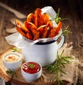 Sweet potato french fries seasoned herbs and sea salt in enamel mug and spicy dips on a wooden table Royalty Free Stock Photo