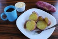 Sweet potato in a white plate with cup of black coffe, bowl of butter and raw potato.