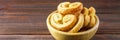 Sweet pretzels made of puff pastry in a bowl on a wooden table banner