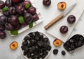 Sweet prunes on plate and scoop with ripe plums in wooden box on light kitchen background Royalty Free Stock Photo