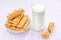 Sweet puff pastry cookies on a white saucer and glass of cow milk over white pink checkered tablecloth. Tasty breakfast with milk Royalty Free Stock Photo