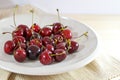 Sweet red cherries on a ceramic plate with a napkin on a light wooden table, healthy summer snack, copy space Royalty Free Stock Photo