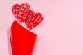 Sweet red lollipops hearts in red paper corner on pastel pink as valentine`s day background.