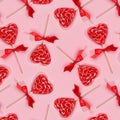 Sweet red lollipops hearts with ribbon on pastel pink as valentines day seamless pattern.