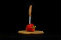 Sweet red pepper with sharp knife is stuck, wooden board and black background Royalty Free Stock Photo