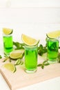 Sweet refreshing mint liqueur, with ice and mint leaves on table background, Shots with lime slice and mint flat lay