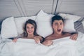 Sweet revenge. Top view of unhappy, screaming husbans and laughing wife lying in bed covered by sheets looking at camera, she mad Royalty Free Stock Photo