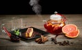 Sweet rolls in black plate with sauce and mint sprig. Teapot full of hot citrus tea steaming on table. Dark background.