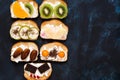 Sweet sandwiches with cream cheese and fruit-kiwi, orange, physalis, pineapple, pear, chocolate, dates. Blue dark background, top Royalty Free Stock Photo