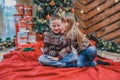 Sweet shot of a girl telling a secret in the ear to her brother sitting on red blanket at home, celbrating Christmas.