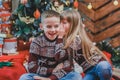 Sweet shot of a girl telling a secret in the ear to her brother sitting on red blanket at home, celbrating Christmas.