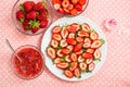 Sweet sliced strawberries on a plate, strawberry jam in a glass bowl, and other sweet berries