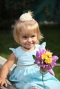 Sweet smiling little girl with long blond hair, sitting on grass in summer park, closeup outdoor portrait. Royalty Free Stock Photo