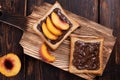 Sweet snack, chocolate paste toast with peach slices on a plate on a cutting board on a dark wooden background Royalty Free Stock Photo