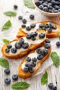 Sweet toasts with creamy vanilla cheese fresh blueberries honey and cinnamon on a wooden table.